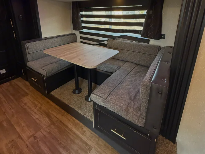 Cozy RV rental dinette featuring L-shaped seating, a light table, window blinds, and under-seat storage for your travels.. Forest River Cherokee Grey Wolf 2021