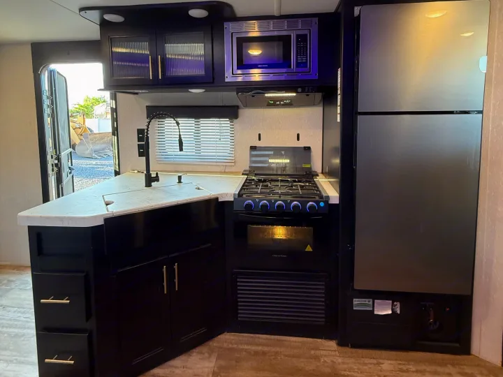 Inside a modern RV rental: sleek black kitchen with stainless steel appliances including microwave, stove, sink, and fridge.. Forest River Cherokee Grey Wolf 2021