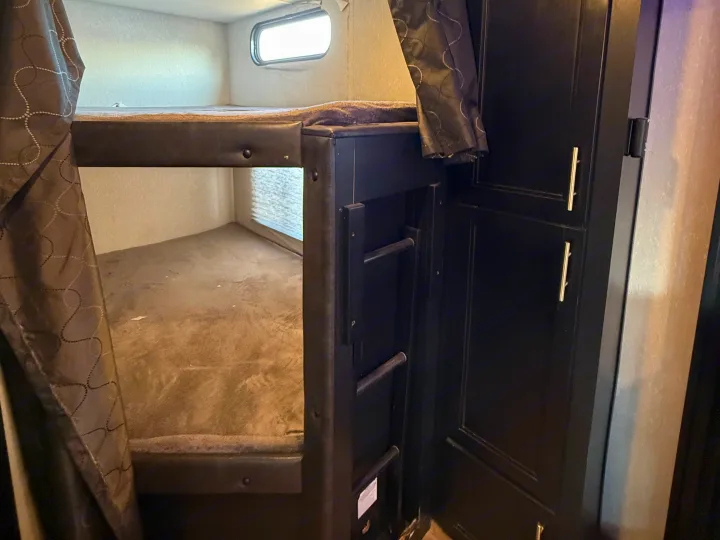 Inside an RV rental: a bunk bed sleeping area with a small ladder, window, and cabinet storage.. Forest River Cherokee Grey Wolf 2021
