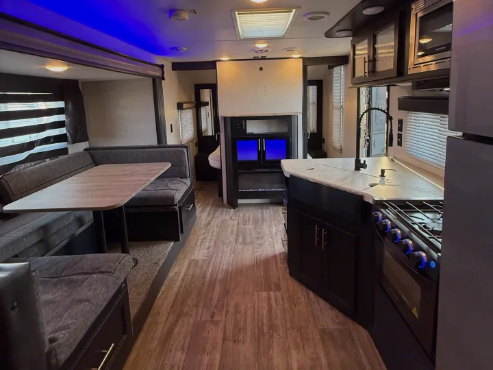 This modern RV rental interior features a spacious kitchen, dining area, and living space with blue accent lighting and wood-look flooring.. Forest River Cherokee Grey Wolf 2021