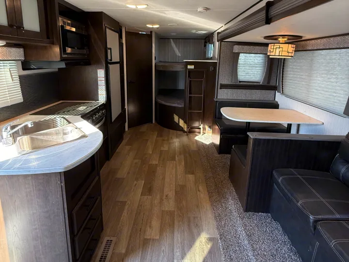 Inside this RV rental: kitchen with microwave & stove, dinette, and bunk beds in a cozy, well-lit space.. Heartland RVs Pioneer 2021