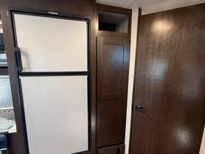 RV rental interior features a Dometic refrigerator, pantry cabinet, and a wooden interior door, showcasing compact design.. Heartland RVs Pioneer 2021