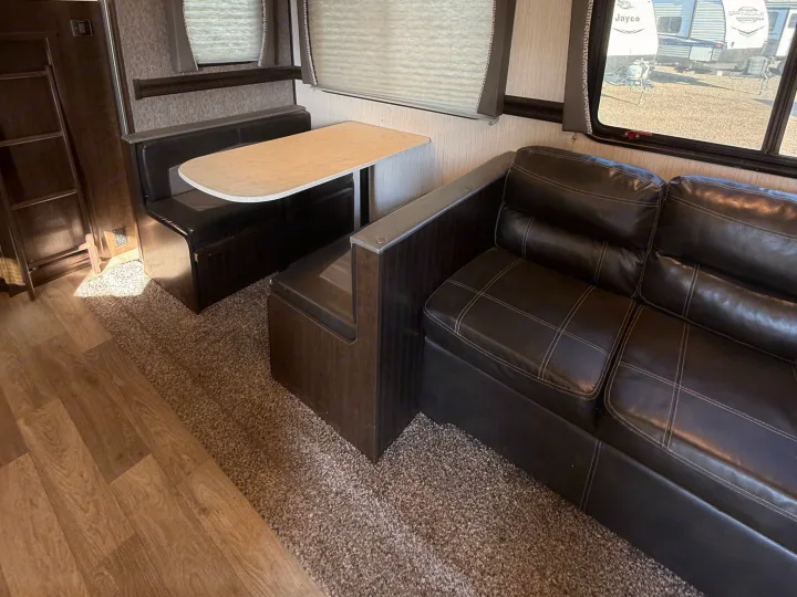 Inside an RV rental: a compact travel trailer living space with a cozy dinette, comfortable sofa, and mixed flooring.. Heartland RVs Pioneer 2021