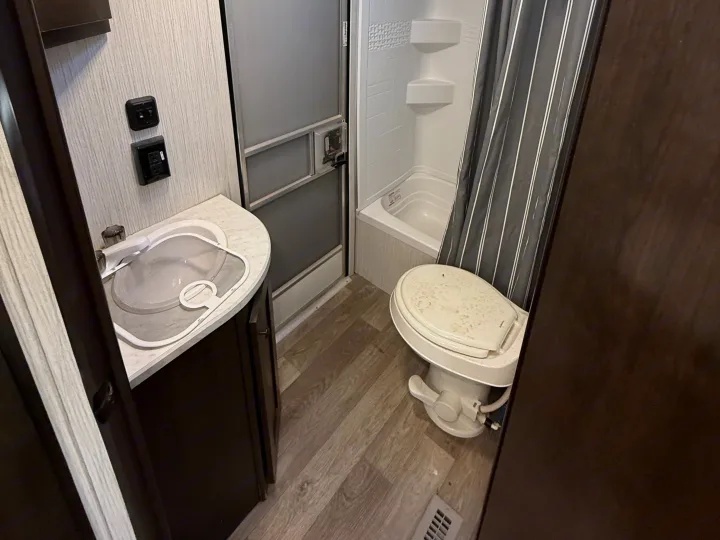 Compact RV rental bathroom showing a white sink, toilet, and shower/tub with a striped curtain.. Heartland RVs Pioneer 2021
