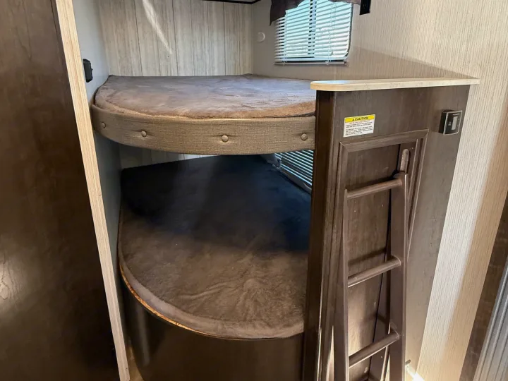 RV rental featuring stacked bunk beds with cushions and a side ladder. A window with blinds is visible above the top bunk.. Heartland RVs Pioneer 2021