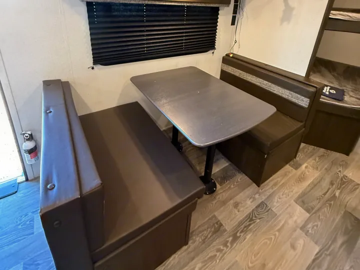 RV rental dinette with dark benches, gray table, light walls, and wood-look floor. Compact camper dining area.. Keystone RV Springdale 2021
