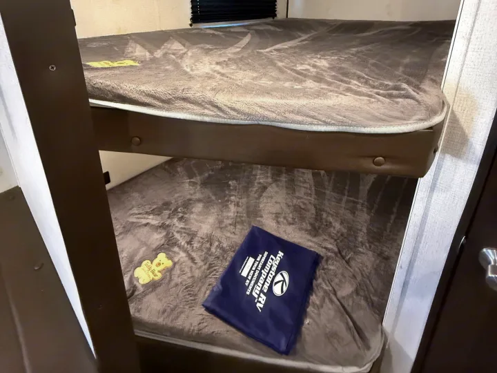 Cozy bunk beds in an RV rental, featuring Keystone RV documents and a cute "Teddy Bear" tag on the lower bunk. Perfect for family camping.. Keystone RV Springdale 2021