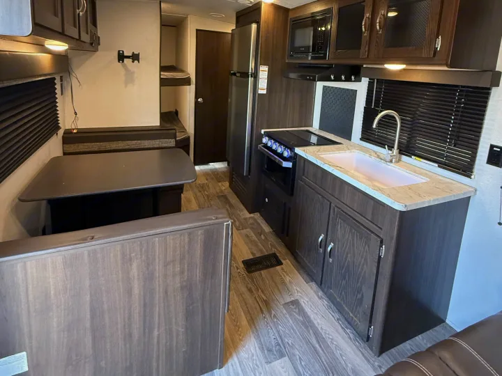 Spacious rv rental interior with kitchenette, dinette, bunk beds, wood cabinetry, and laminate flooring.. Keystone RV Springdale 2021