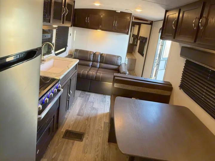 RV rental interior with a compact kitchen, including a fridge, sink, and stovetop, and a living area with a sofa and dining table.. Keystone RV Springdale 2021