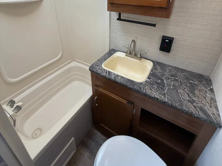 Inside this RV rental's compact bathroom: white tub/shower, vanity with dark marbled countertop, light sink, and toilet.. Keystone RV Springdale SRT 2016