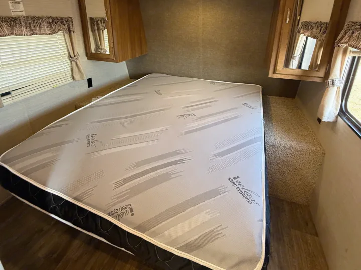 This RV rental bedroom features an iRelax Sleep Systems mattress, window with blinds, and wooden cabinets for a comfortable stay.. Keystone RV Springdale SRT 2016