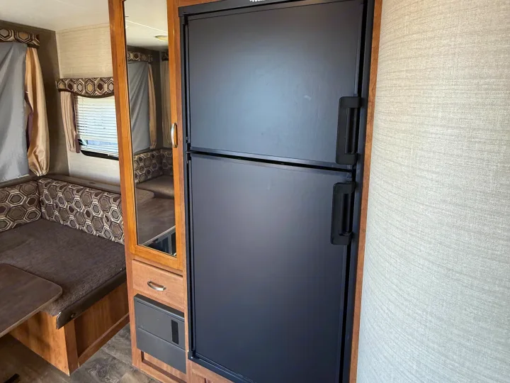 RV rental interior: black fridge, dinette with patterned cushions, a mirror in a cabinet, and an electrical panel.. Keystone RV Springdale SRT 2016