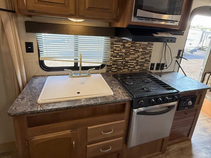 Compact RV rental kitchen with a covered sink, stovetop, oven, microwave, wood cabinets, mosaic backsplash & patterned counters.. Keystone RV Springdale SRT 2016