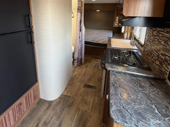 RV rental interior: A compact space showing a black refrigerator, a kitchenette with stove & sink, and a bedroom with a bathroom entrance.. Keystone RV Springdale SRT 2016
