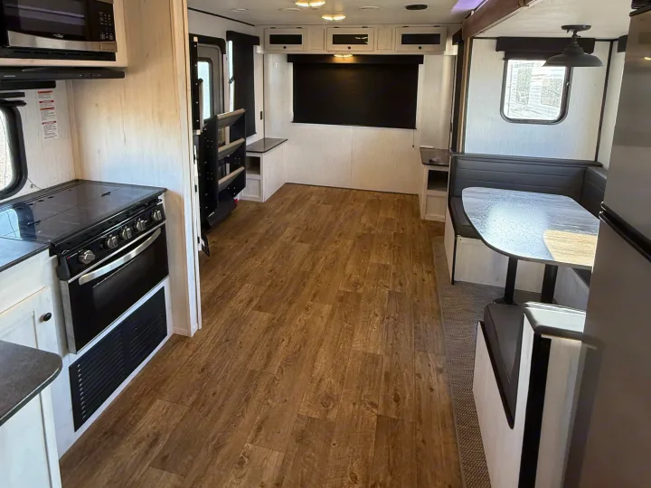 Spacious RV rental interior featuring a full kitchen with stove and microwave, a cozy dinette, and light wood-look flooring.. Heartland RVs Trail Runner 2022