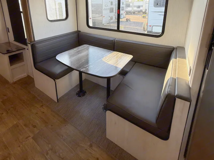 This RV rental features a dinette with dark gray U-shaped benches, a marbled table, and sunlit windows showing other RVs.. Heartland RVs Trail Runner 2022