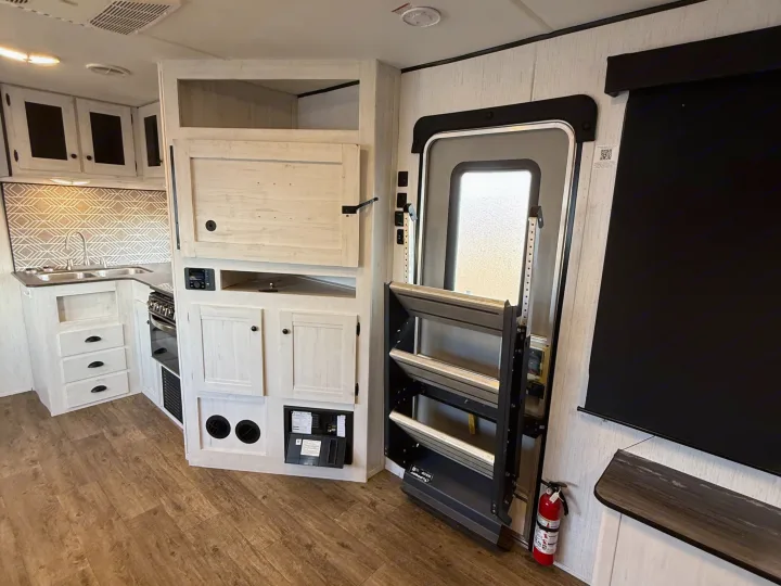 Bright RV rental interior: compact kitchen, storage, main entrance with steps, and a fire extinguisher beside the door.. Heartland RVs Trail Runner 2022