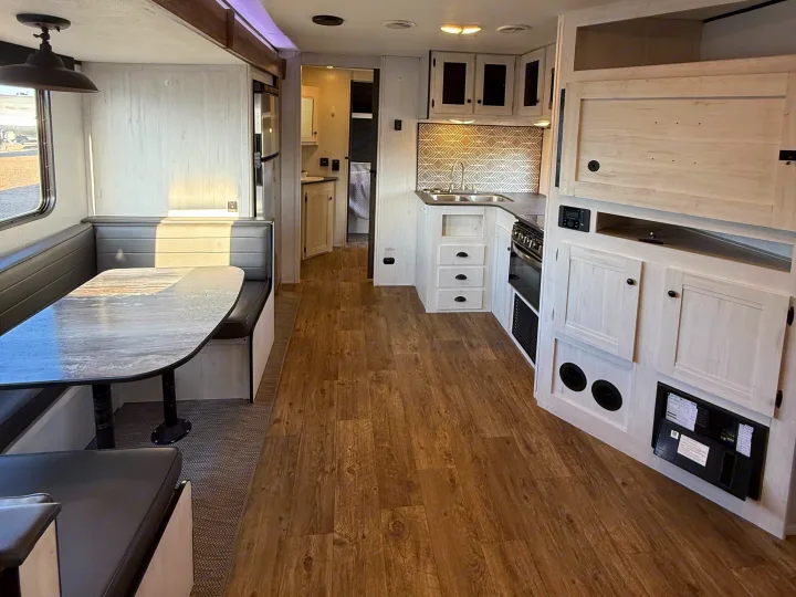 Modern RV rental interior showcasing a bright dinette, a well-equipped kitchen with a sink and stove, and light wood finishes.. Heartland RVs Trail Runner 2022