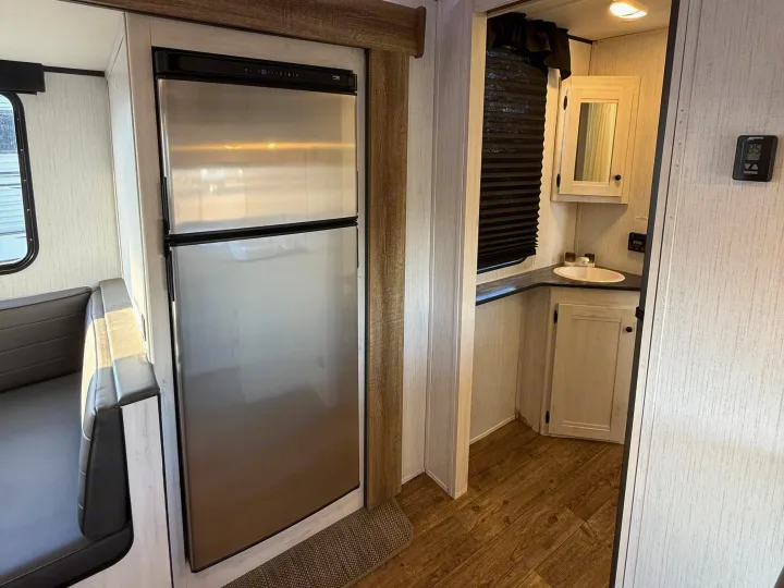 This RV rental interior features a stainless steel fridge, comfortable dinette seating, and a compact bathroom with a sink and mirror.. Heartland RVs Trail Runner 2022
