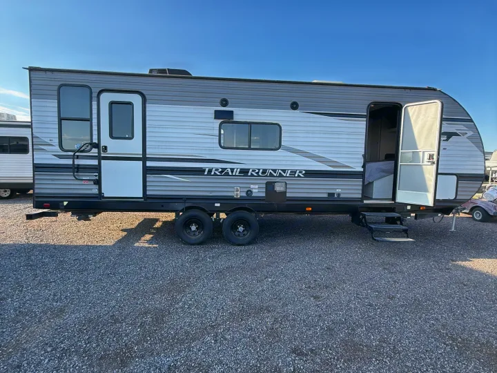 A sleek gray Trail Runner travel trailer, perfect for an rv rental, sits on gravel. Features an open door with steps.. Heartland RVs Trail Runner 2022