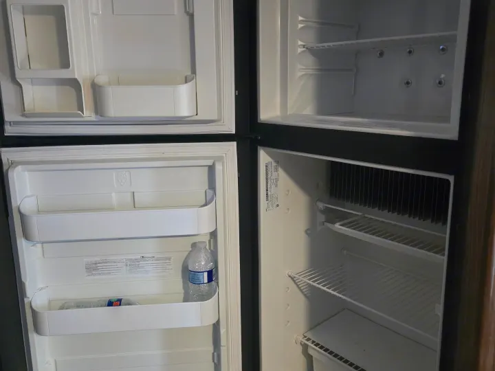 Open, compact two-door refrigerator in an RV rental, with empty shelves & door storage. Ready for provisions.. Coachmen Apex 2017