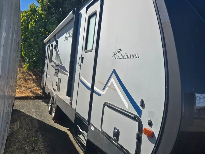 Gray Coachmen Apex RV rental parked outdoors. Side view shows its entry door, awning, and graphic design.. Coachmen Apex 2017