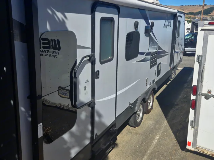 A grey Apex Ultra-Lite travel trailer RV rental, parked with side graphics, a door, and wheels visible.. Coachmen Apex 2017