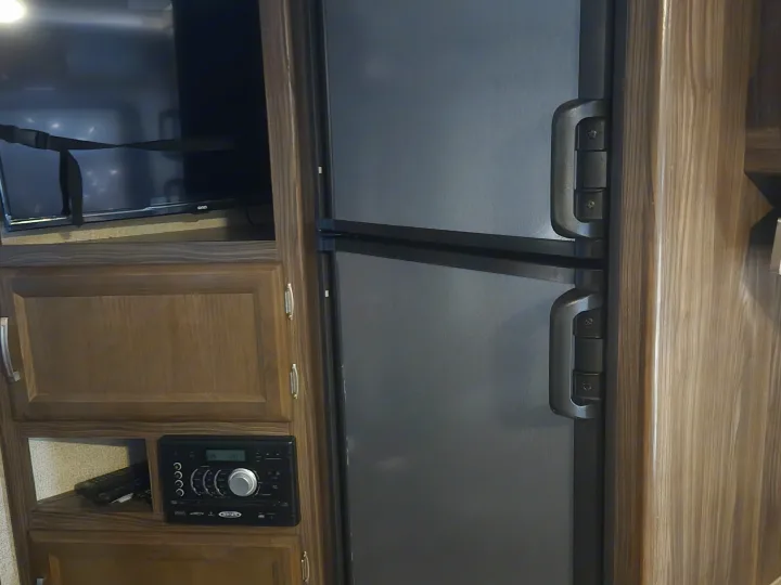 RV rental interior featuring a TV, two-door fridge, and stereo system within wooden cabinetry.. Coachmen Apex 2017