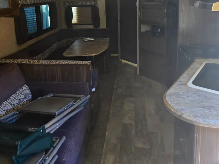 RV rental interior featuring a dinette, kitchen with stovetop, and a living area with folding chairs stored on the sofa.. Coachmen Apex 2017