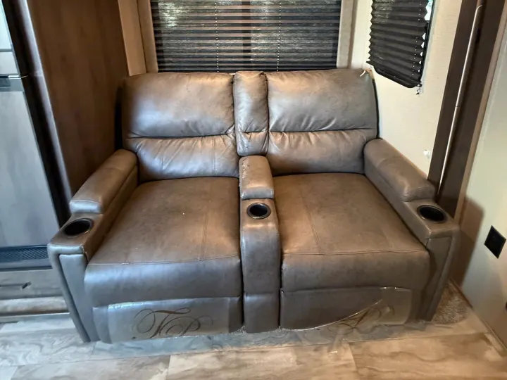 Gray two-seat recliner sofa with cup holders in an RV rental, featuring blinds and laminate flooring.. Grand Design Transcend Xplor 2022