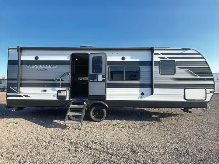 Modern white, black, and gray Transcend Xplor RV rental. Travel trailer on gravel under clear sky, door open.. Grand Design Transcend Xplor 2022