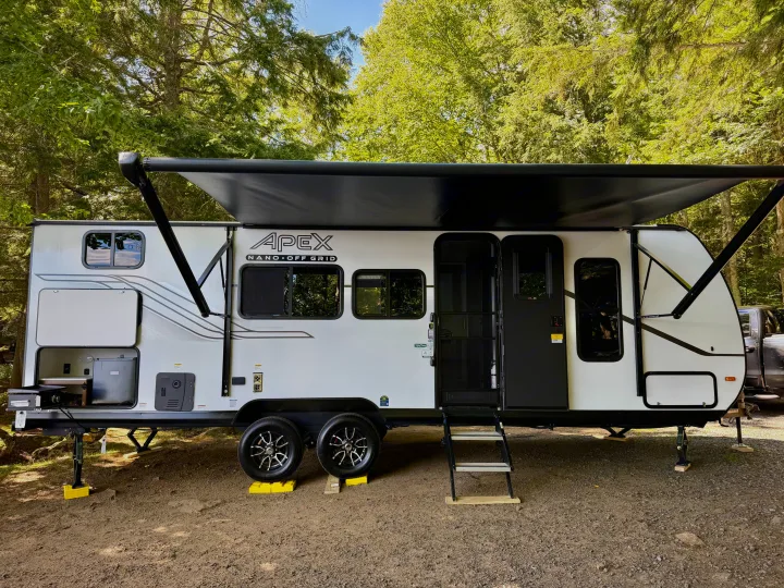 White Apex Nano Off Grid travel trailer set up in a lush forest. This rv rental is ready for your next outdoor adventure.. Coachmen Apex Nano 2026