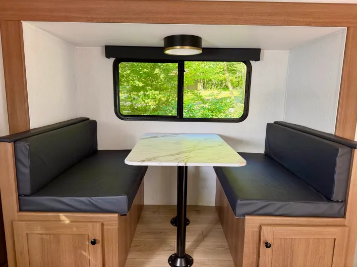 Cozy RV rental dinette featuring black cushioned benches, a marble-style table, and a window view of lush greenery.. Coachmen Apex Nano 2026