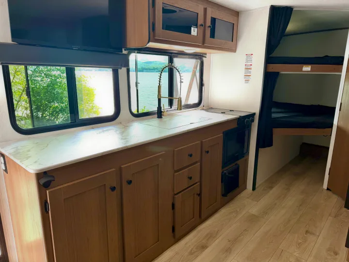 RV rental interior: Modern kitchen with gold faucet, stove, microwave, lake view, and cozy bunk beds visible.. Coachmen Apex Nano 2026