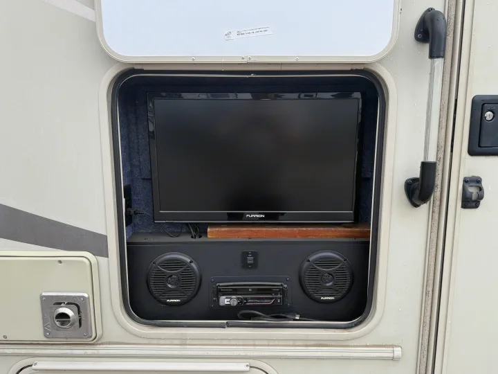 RV rental with Furrion outdoor entertainment system: TV, speakers, and stereo in an open compartment for campsite fun.. Coachmen Leprechaun 240FS 2018