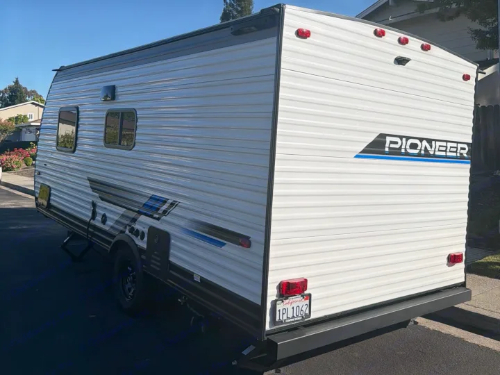 This white Pioneer travel trailer RV rental, parked on asphalt, offers a clear view of its side and rear.. Heartland RVs Pioneer 2025