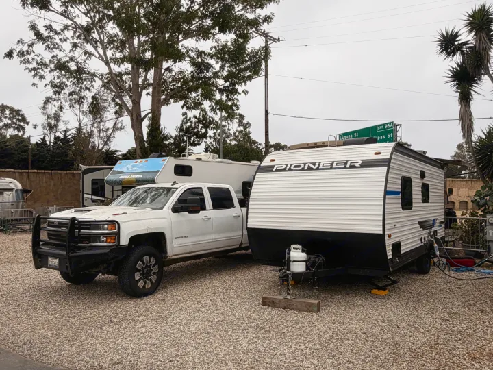 A white pickup truck is hitched to a Pioneer travel trailer at an RV rental campground, with other RVs nearby.. Heartland RVs Pioneer 2025
