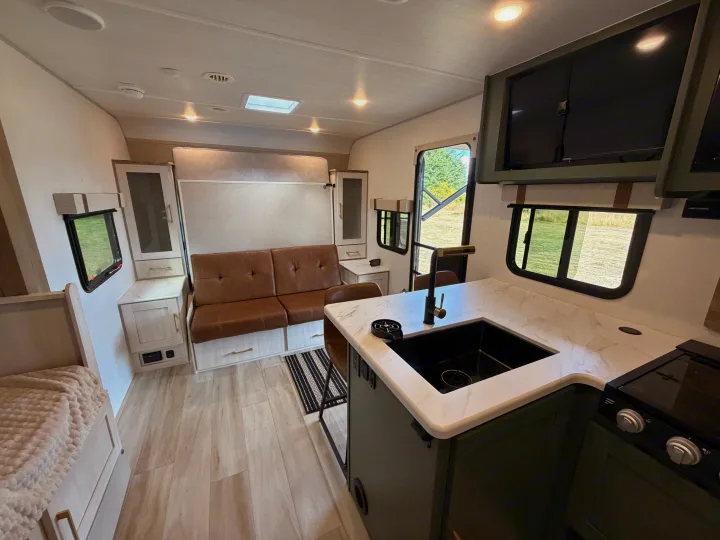 Modern and bright RV rental interior with a cozy sofa, kitchen, and entertainment TVs, perfect for travel adventures.. No Boundaries 20 2026