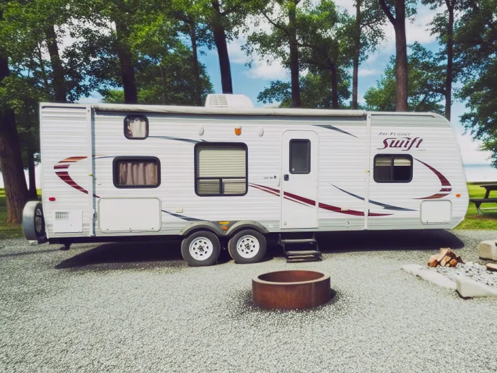 This RV rental, a Jay Flight Swift travel trailer, is set up at a gravel campsite with a fire pit, surrounded by trees.. Jayco Jay Flight Swift 2014