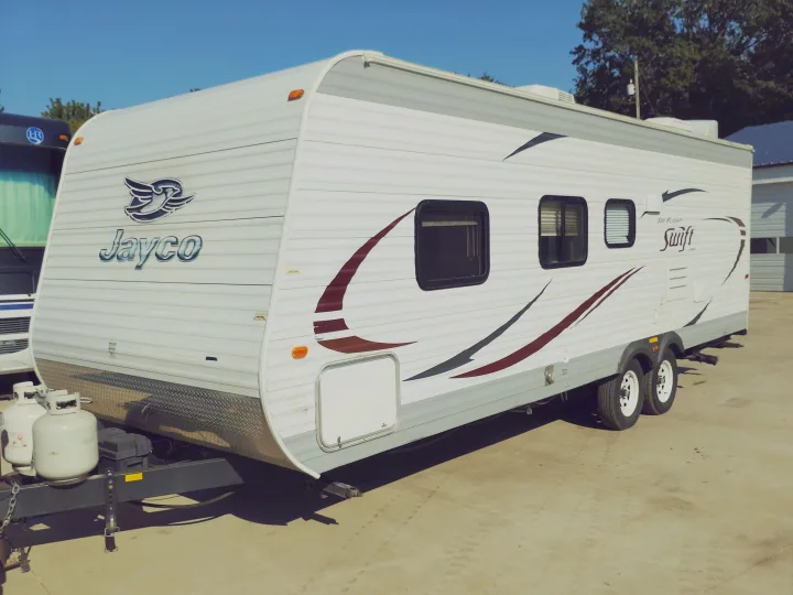 White Jayco Swift travel trailer RV rental, featuring maroon and black graphics, parked on a concrete surface, ready for camping.. Jayco Jay Flight Swift 2014