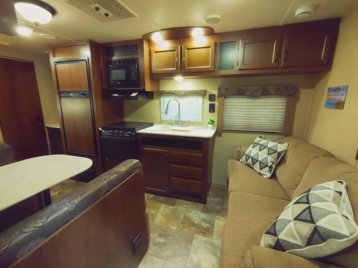 An RV rental interior featuring a kitchen with a fridge, stove, and microwave, plus a dinette and sofa.. Jayco Jay Flight Swift 2014