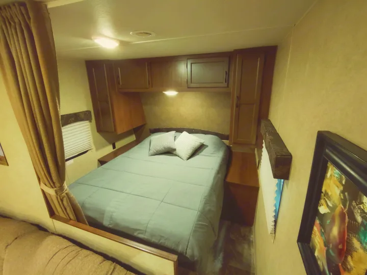 Cozy rv rental bedroom features a queen bed, overhead cabinets, a window with blinds, and soft lighting.. Jayco Jay Flight Swift 2014