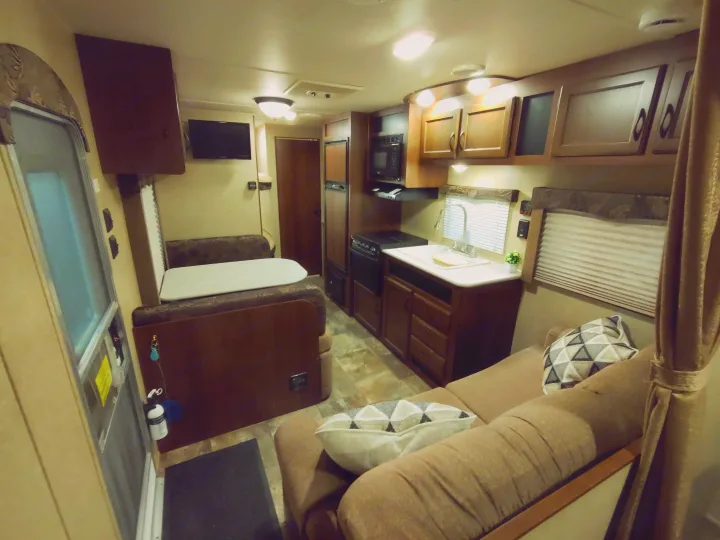 Inside a modern rv rental: kitchen with sink & stove, dinette, cozy couch, and mounted TV. Warm, inviting camper interior.. Jayco Jay Flight Swift 2014