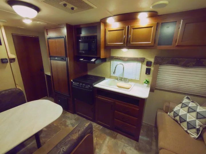 This rv rental interior features a compact kitchen with a sink, stove, microwave, and fridge, a dining table with bench seating, and a sofa.. Jayco Jay Flight Swift 2014