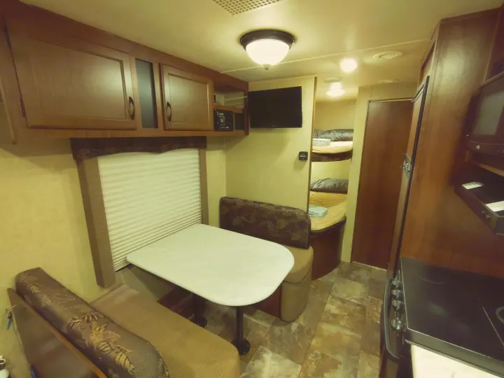 RV rental interior features a dinette, overhead cabinets, TV, and a glimpse into the bunk bed area. Ideal for family adventures.. Jayco Jay Flight Swift 2014
