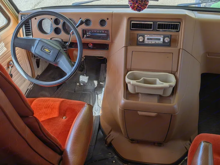 Vintage RV rental interior: classic Chevy dash, orange seats, and retro radio, ready for your next adventure.. Chevrolet Vanguard 1980