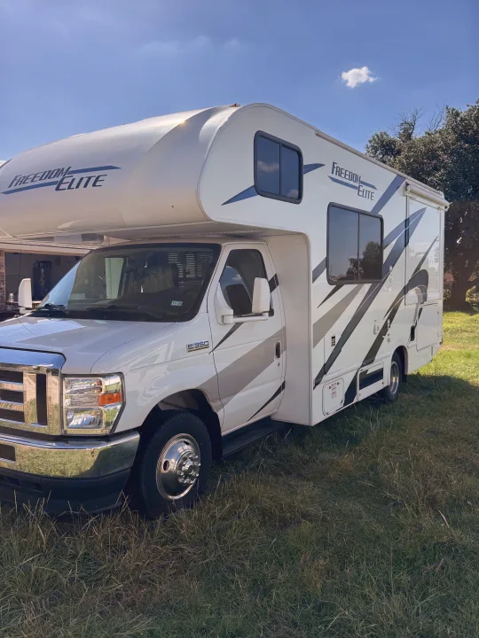 White Freedom Elite Class C RV rental parked on grass under a clear sky. Perfect for your next adventure.. Thor Freedom Elite 2023