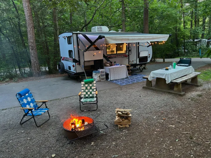 Relaxing at an RV rental campsite in a forest with a warm fire pit and illuminated outdoor living space.. Forest River Wildwood FSX Platinum 2021