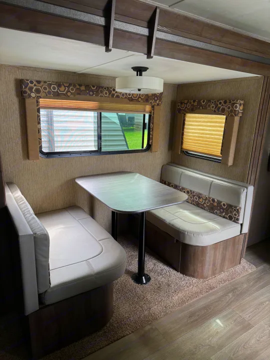 Cozy dinette inside an RV rental, featuring light gray benches, a modern table, and windows with patterned valances.. Dutchmen Coleman Light 2019