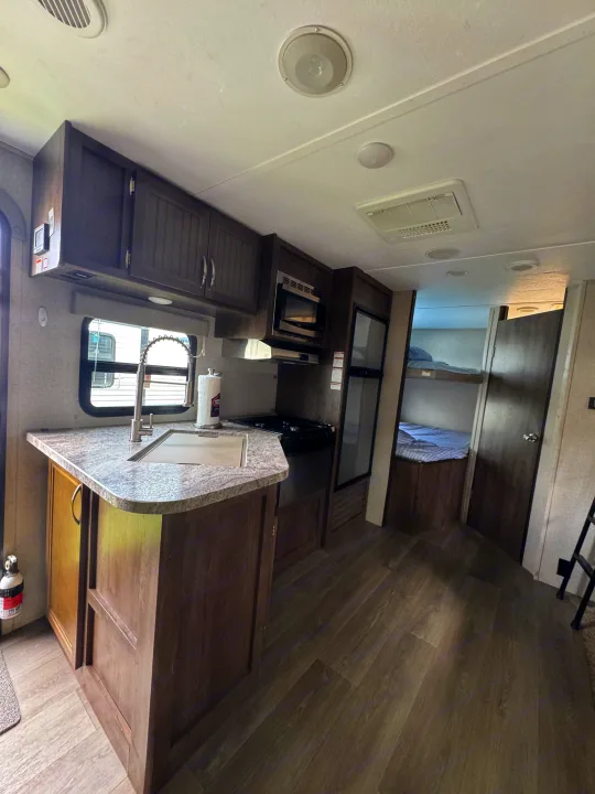 Spacious rv rental kitchen with sink, stove, microwave, and fridge, leading to bunk beds. Modern interior design.. Dutchmen Coleman Light 2019